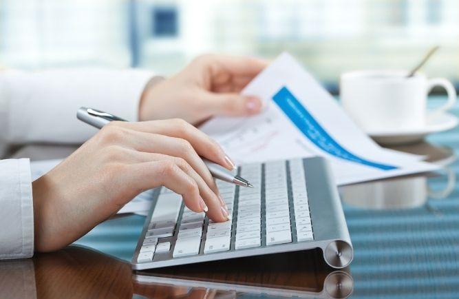 person is on the computer and punching in numbers from a report for a client